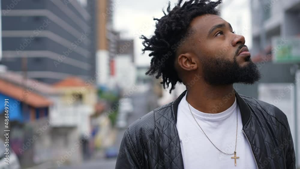 A pensive African American man looking up to sky in contemplation standing by urban street