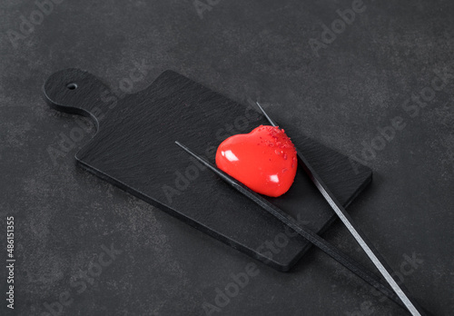 Modern dessert in the shape of a heart with a red mirror chocolate glaze on a serving board on a dark background. Valentine's day