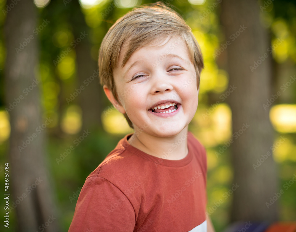 Cheerful and happy little boy. He is smiling against the background of the park Cheerful and happy little boy. He is smiling against the background of the park