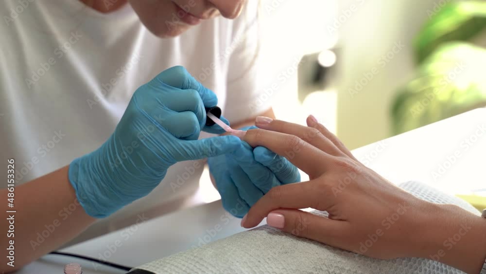 Professional manicure master with gloves applies pink varnish to nails during the manicure procedure. Small business in covid 19 pandemic. close up view. 4k footage Professional manicure master with gloves applies pink varnish to nails during the manicure procedure. Small business in covid 19 pandemic. close up view. 4k footage