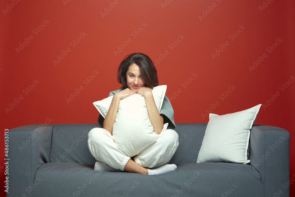 Pleased stylish young woman brunette hug white pillow sitting on cozy sofa, resting, relaxing on weekend Pleased stylish young woman brunette hug white pillow sitting on cozy sofa, resting, relaxing on weekend