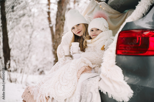 Two little girs by car in the winter forest photo