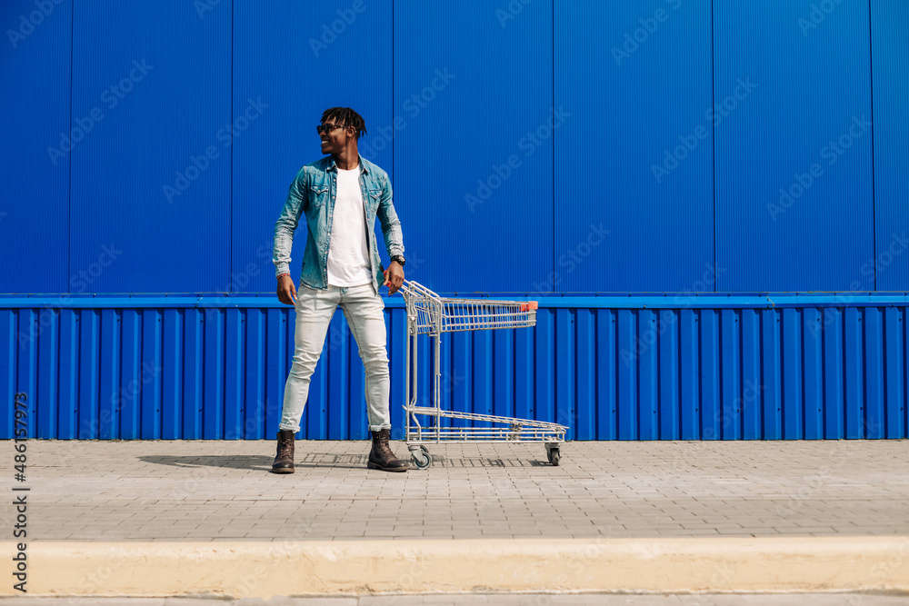 African American man shopping in push cart supermarket. Side view of a cheerful young man, with a shopping trolley