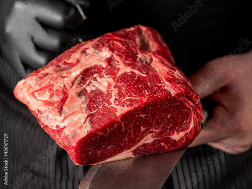 Close up beef meat in chef butcher's hands with knife on black background