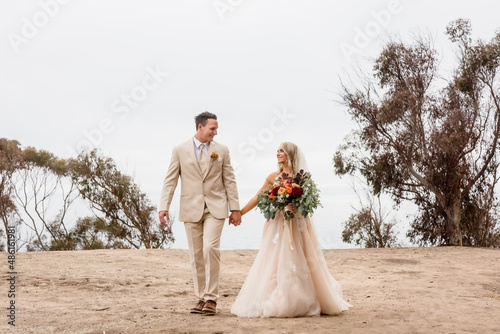  Bride and Groom walking holding hands on a cliff overlooking the pacific ocean in La Jolla California