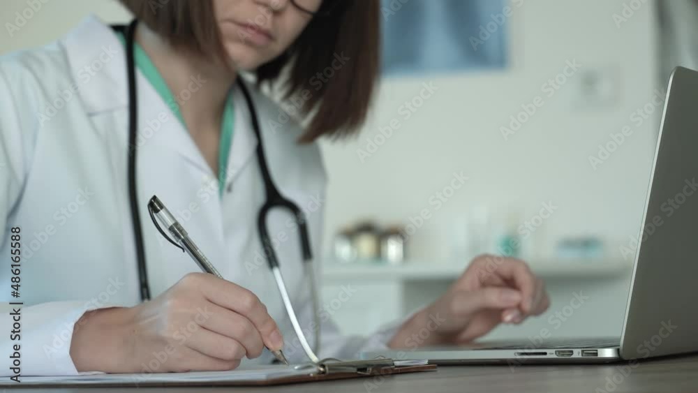Caucasian young female doctor in surgeon coat and glasses capturing medical data on laptop. Social network. Telemedicine, Remote. Distance consultation. remote healthcare services. 4k footage Caucasian young female doctor in surgeon coat and glasses capturing medical data on laptop. Social network. Telemedicine, Remote. Distance consultation. remote healthcare services. 4k footage