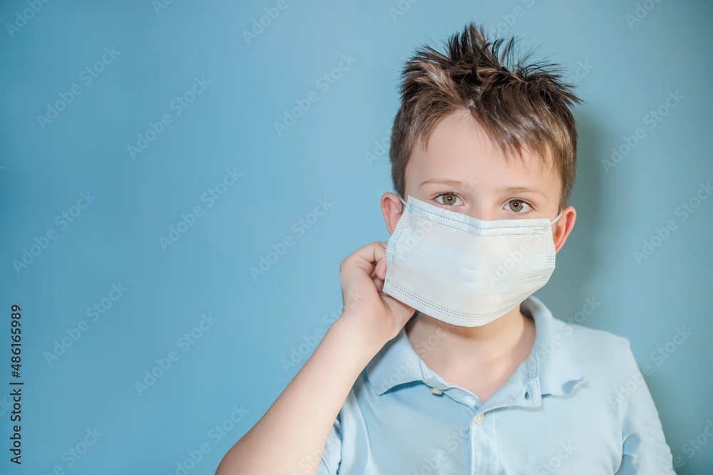 boy puts on a medical protective mask on blue background. child with flu, influenza or cold protected from viruses, pollution in bad epidemic situation, among patients with coronavirus boy puts on a medical protective mask on blue background. child with flu, influenza or cold protected from viruses, pollution in bad epidemic situation, among patients with coronavirus