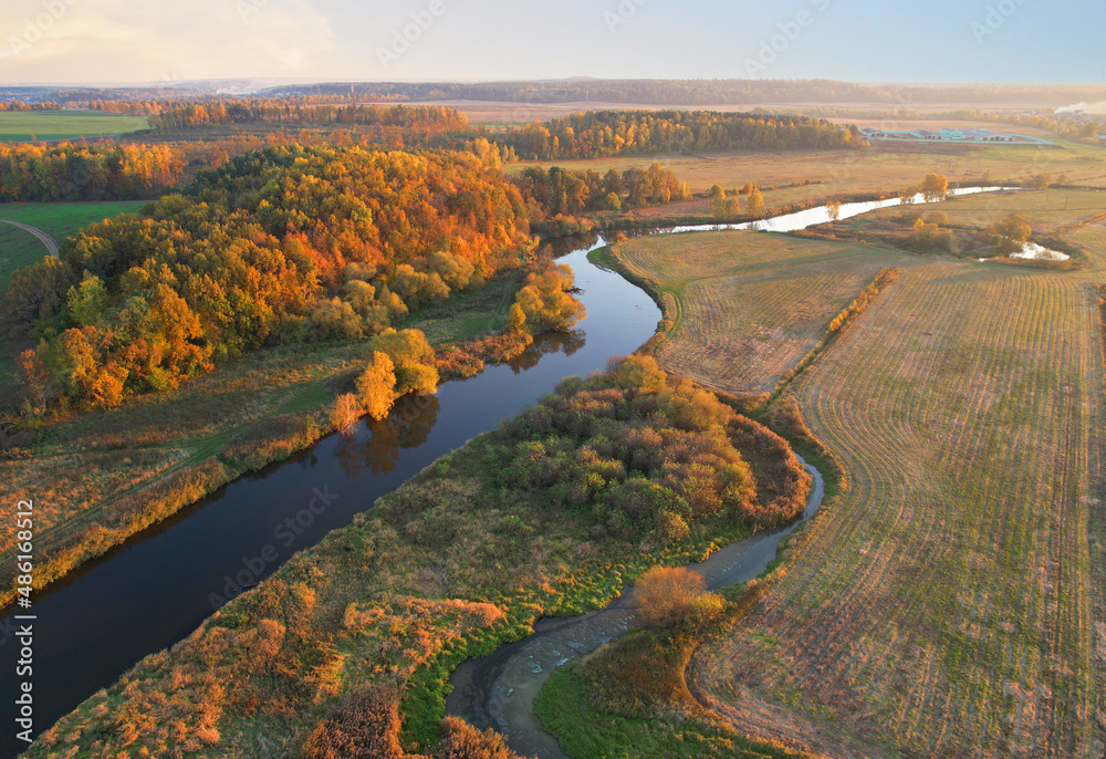 River at field in the fall season. Golden autumn landscape. Aerial view of the wild river on sunset in autumn season. Trees with yellow leaves at a small winding river. Aerial panoramic landscape. 