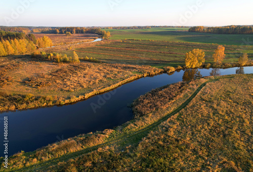 River at field in the fall season. Golden autumn landscape. Aerial view of the wild river on sunset in autumn season. Trees with yellow leaves at a small winding river. Aerial panoramic landscape.
