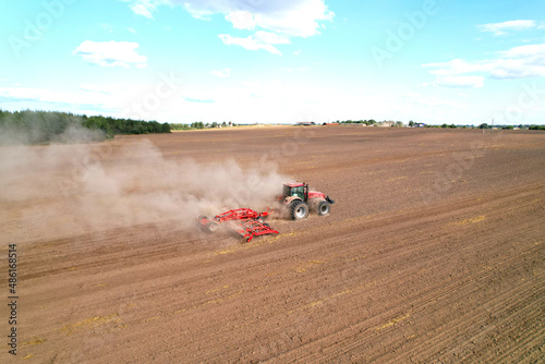 Field cultivating, aerial view. Tractor with disk harrow on plowed. Arable land ploughed and soil Tillage. Agricultural Tractor with plough on field cultivating. Red tractor on sowing seeds..
