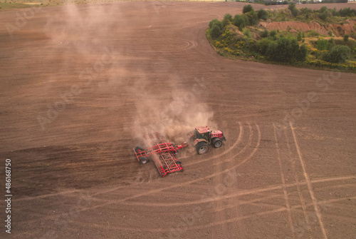 Field cultivating, aerial view. Tractor with disk harrow on plowed. Arable land ploughed and soil Tillage. Agricultural Tractor with plough on field cultivating. Red tractor on sowing seeds..