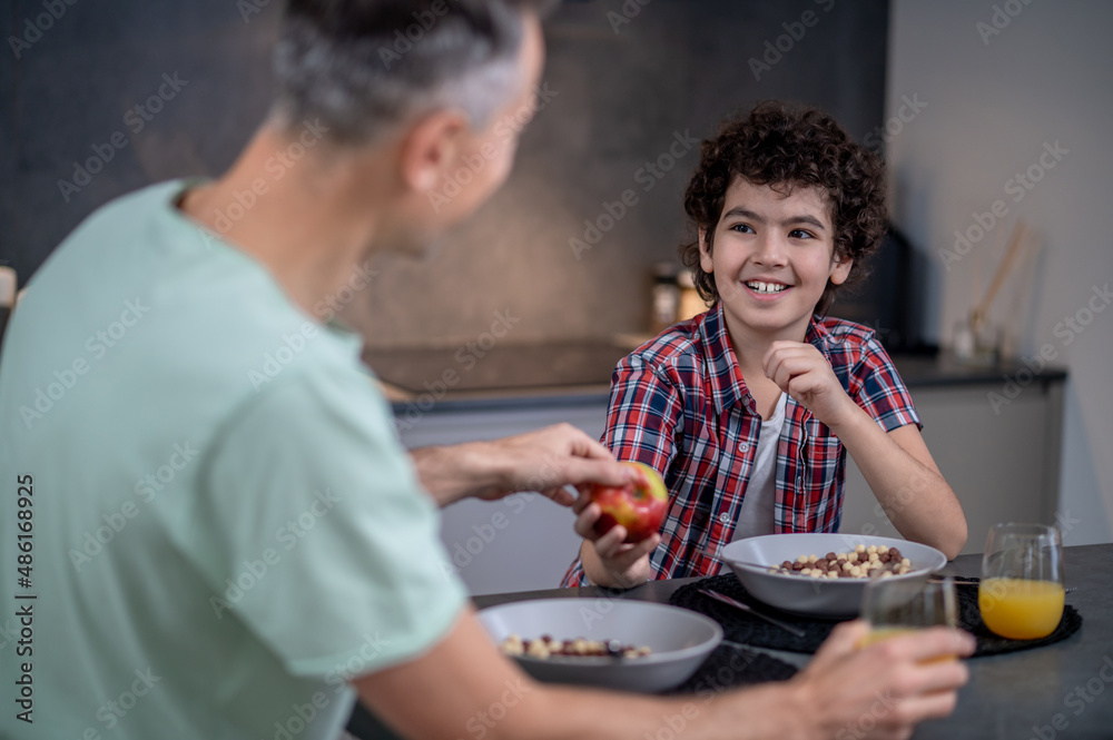 Boy treating father with apple sitting at table