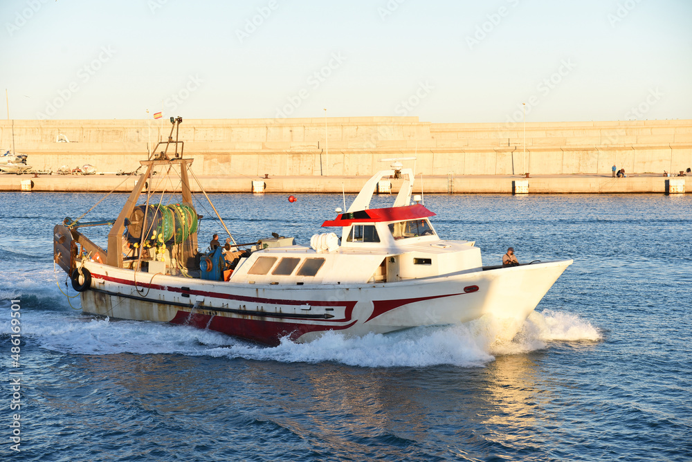 Fishing boat enters the in La Marina de Valencia. Fishermen on a fishing boat deliver the caught fish to the port. Fishing motorboat at Mediterranean Sea. Skiff at ​Dock..