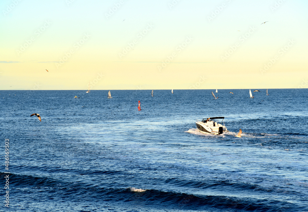 Obraz premium Motor boat in the sea at sunset. Yacht and motorboat on waves in Mediterranean Sea. Skiff and Sailboat in ocean. Yachting and sailing sport. Speedboat or powerboat on the waves near the Spanish coast.