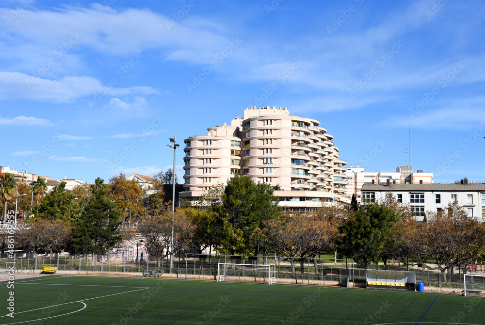 Football stadium in the city park in Valencia. View of a sports stadium with a green lawn against the backdrop of residential buildings. Sports field for playing ball. Small soccer stadium in town.