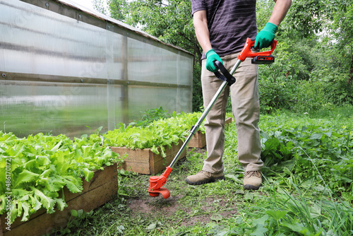 Portable trimmer for cutting grass and undesirable plant in hands of person In action 