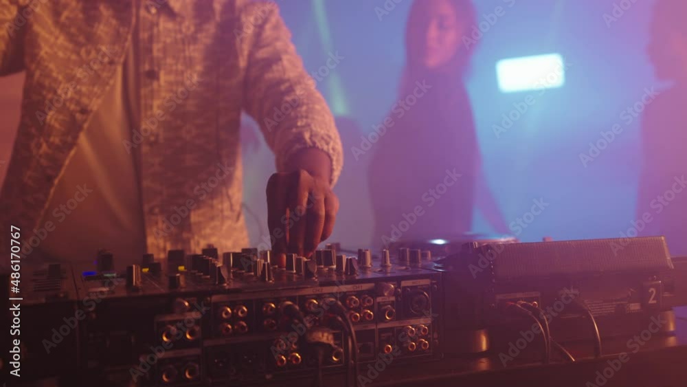 Close-up of technic equipment, DJ controlling mixing desk. Tilt up reveal dancing people. Nightlife, modern music and entertainment concept.