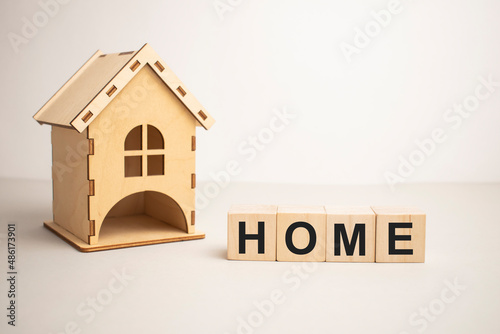 Wooden house and cube blocks spelling HOME on wood board. Concept for financial home loan or money saving for house buying.