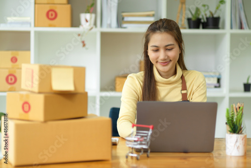 Female entrepreneur working on a laptop in a room full of delivery packages.