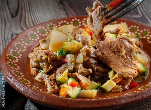 Boneless chicken legs with onions, red peppers, zucchini, garlic, potatos and condiments, on a mexicna mud plate, with a fork taking a piece of chicken photo