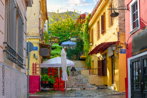 A colorful hillside alley in the Plaka district of Athens, Greece, with cafes and shops at the base of the ancient Acropolis.