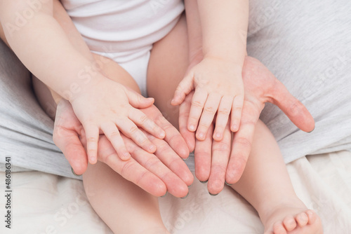 Fototapeta Naklejka Na Ścianę i Meble -  Hands of a mother and a small child, close-up, light colors. Mom hugs the baby. The concept of maternal, parental love and care. Background for Mother's Day and child's Day