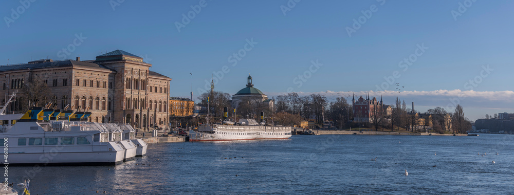 Panorama view over the bay Strömmen and the islands Blasieholmen with commuting steam boats at a pier and hotels and museums, the former military buildings and museums a sunny winter day in Stockholm