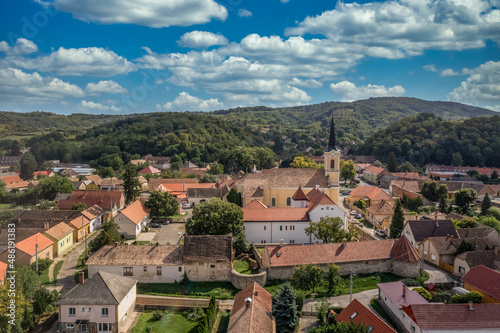 Aerial view of Szaszvar castle and fortified manor house, church in Baranya county Hungary with newly renovated Gothic palace, red shingle roof, white walls blue cloudy sky