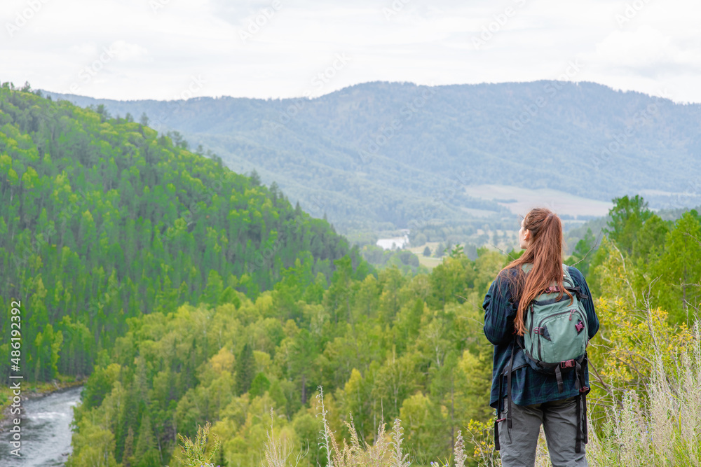 Young woman with backpack enjoys the view of nature at hike. Empty space for text. Back view