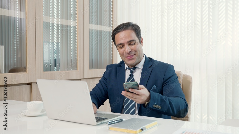 Business man sitting using laptop study online work at his desk success celebration at office, Smiling happy businessman cheerful in casual office making phone call while working with laptop computer Business man sitting using laptop study online work at his desk success celebration at office, Smiling happy businessman cheerful in casual office making phone call while working with laptop computer