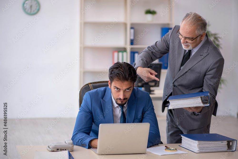 Old male boss and young male employee working in the office Old male boss and young male employee working in the office