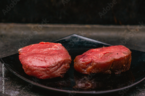Two pieces of raw beef on a plate on dark background