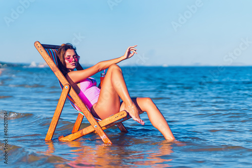 Side view of pretty girl in a pink bathing suit relaxing on the beach while lying at the deck chair