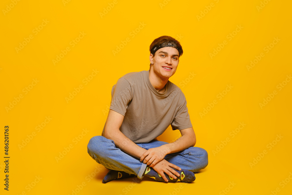 Happy young man in casual clothes sitting on the floor in bright yellow studio Happy young man in casual clothes sitting on the floor in bright yellow studio