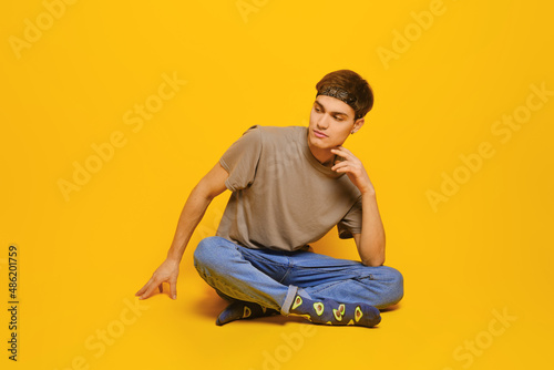 Cheerful young man in casual clothes sitting on the floor in bright yellow studio © boomeart