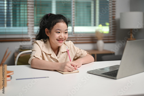 Smiling asian girl studying online with laptop computer at home.
