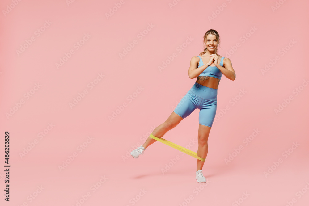 Full body young happy fun sporty athletic fitness trainer instructor woman wear blue tracksuit spend time in home gym use fitness rubber bands isolated on plain pink background. Workout sport concept.