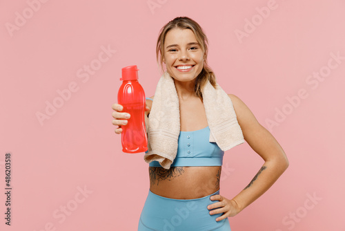 Young sporty athletic fitness trainer instructor woman wear blue tracksuit spend time in home gym give water bottle isolated on pastel plain light pink background. Workout sport motivation concept