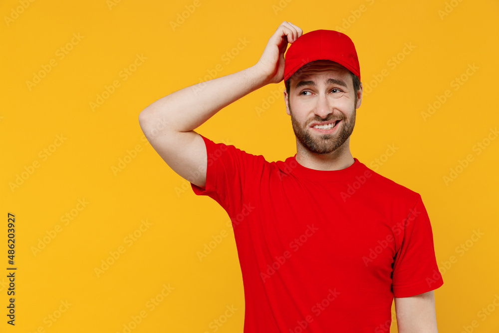 Professional sad delivery guy employee man in red cap T-shirt uniform workwear work as dealer courier scratch hold head look aside isolated on plain yellow background studio portrait. Service concept.