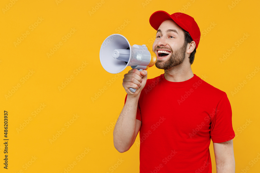 Delivery guy employee man wear red cap T-shirt uniform workwear work as dealer courier hold scream in megaphone announces discounts sale isolated on plain yellow background studio. Service concept Delivery guy employee man wear red cap T-shirt uniform workwear work as dealer courier hold scream in megaphone announces discounts sale isolated on plain yellow background studio. Service concept