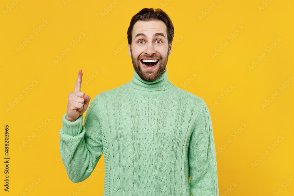 Young insighted smart proactive happy man 20s in mint knitted sweater holding index finger up with great new idea isolated on plain yellow background studio portrait. People lifestyle fashion concept. Young insighted smart proactive happy man 20s in mint knitted sweater holding index finger up with great new idea isolated on plain yellow background studio portrait. People lifestyle fashion concept.
