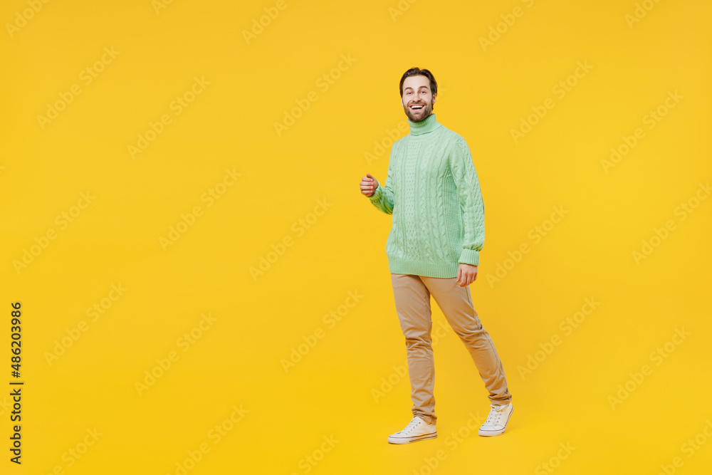 Full body smiling happy young caucasian man 20s wearing mint knitted sweater walking going strolling look camera isolated on plain yellow background studio portrait. People lifestyle fashion concept. Full body smiling happy young caucasian man 20s wearing mint knitted sweater walking going strolling look camera isolated on plain yellow background studio portrait. People lifestyle fashion concept.