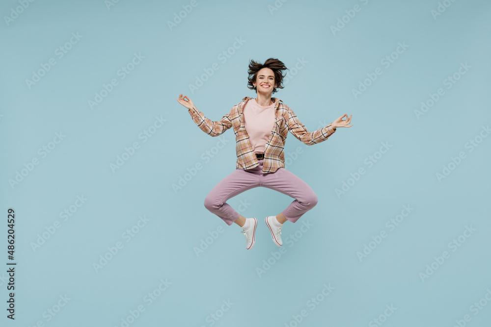 Full body young happy woman 20s in casual brown shirt hold spreading hands in yoga om aum gesture relax meditate try to calm down jump high isolated on pastel plain light blue color background studio Full body young happy woman 20s in casual brown shirt hold spreading hands in yoga om aum gesture relax meditate try to calm down jump high isolated on pastel plain light blue color background studio