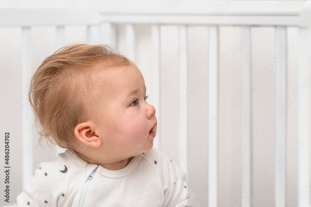 Close up portrait of a serious baby sitting in a white crib