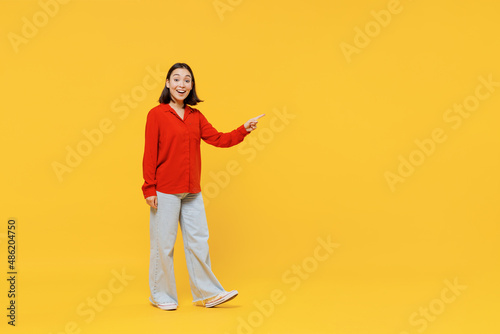 Full size body length happy young woman of Asian ethnicity 20s in casual clothes look camera go move pointing on workspace area copy space mock up isolated on plain yellow background studio portrait.