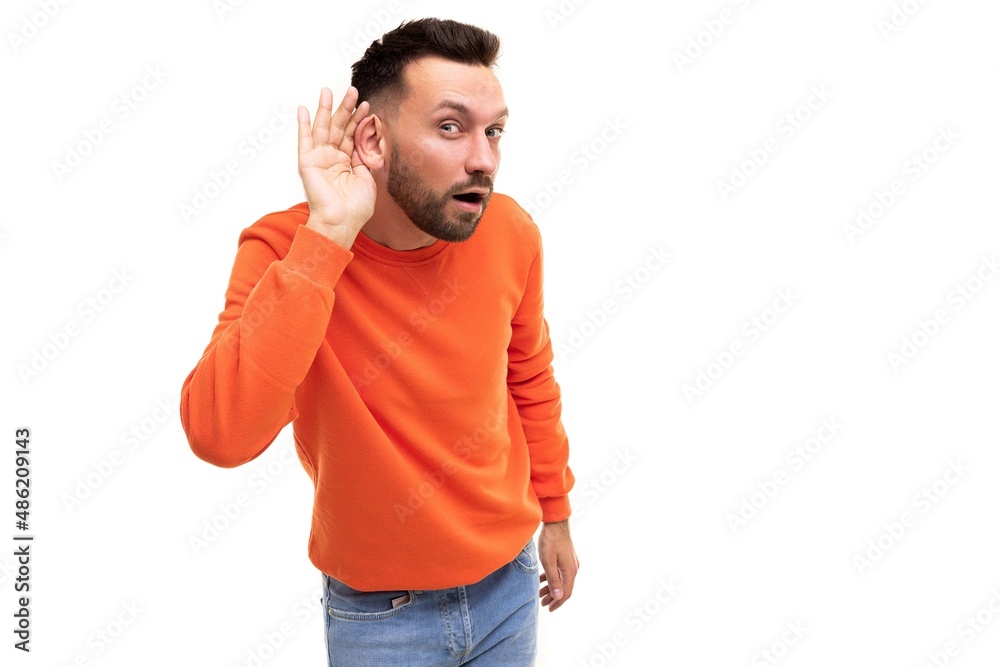 a man in an orange sweater overhears with his hand to his ear on a white background a man in an orange sweater overhears with his hand to his ear on a white background