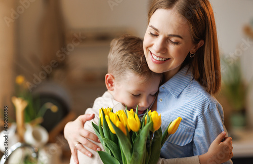 Young  woman mother with flower bouquet embracing son while getting congratulations on Mother's day