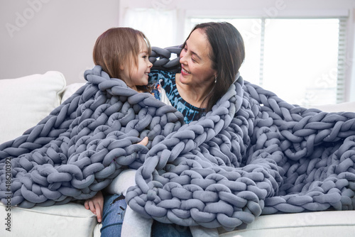 Mother and daughter wrapped in blanket on white couch