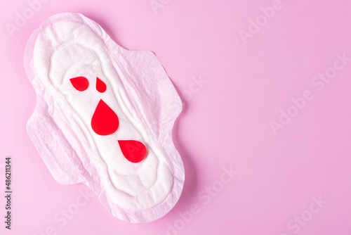 Women's Menstrual pads (sanitary napkin) with red drops on a pink background. The concept of critical days, PMS, menstruation. Space for text. photo