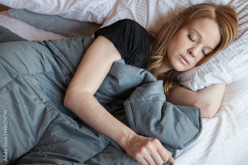 Young redhead woman using soft weighted blanket in her modern apartment while sleeping